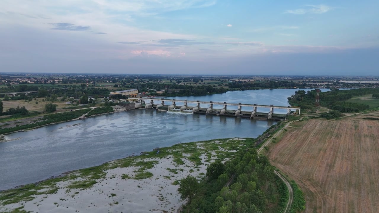 La diga di Isola Serafini attraversa il fiume Po vicino a Monticelli d'Ongina, Piacenza, Emilia-Romagna, Italia, con sponde esposte e condizioni di basso livello dell'acqua durante la siccità del 2026, sorvolo con drone