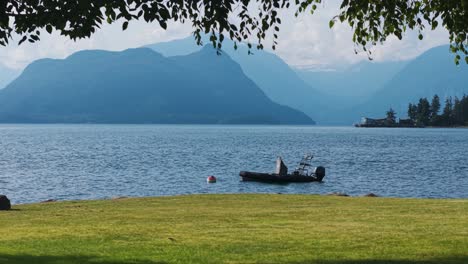 a tranquil blue waters reflects the beauty of nearby mountains while a small fishing boat floats gently on the water. the peaceful grassy shore enhances the serene atmosphere