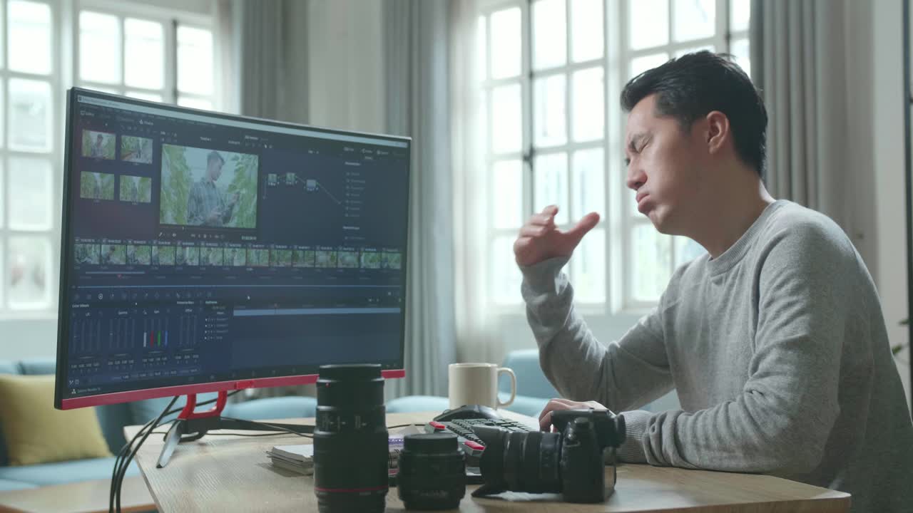 editor de video asiático hombre con camiseta de mangas largas cansado mientras usa computadora de escritorio para editar video en casa.