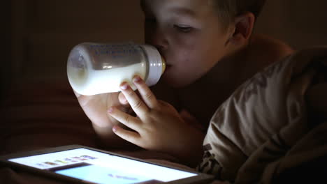 Niño-Bebiendo-Leche-De-La-Botella-Y-Mirando-El-Panel-Táctil