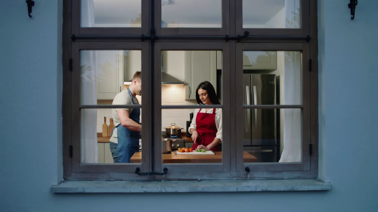 Dinner time bringing couple in blue, red aprons chopping on cutting board, stirring pots in kitchen
