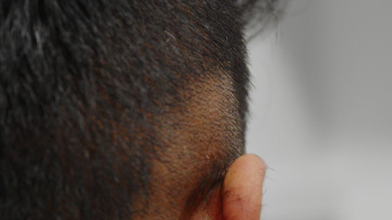 un peluquero limpia el lado desteñido del cabello de otro hombre con cortapelos, afeitándose hasta la piel