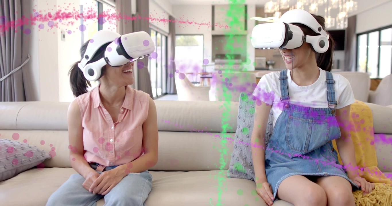Sorelle che indossano visori VR, avviano una demo e si danno il cinque tra particelle rosa e verdi vorticose in un ambiente tecnologico.