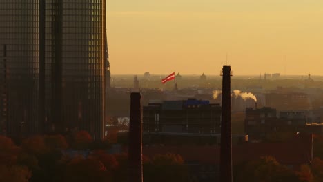 drone glides left past riga’s chimneys with waving latvian flag and golden sky
