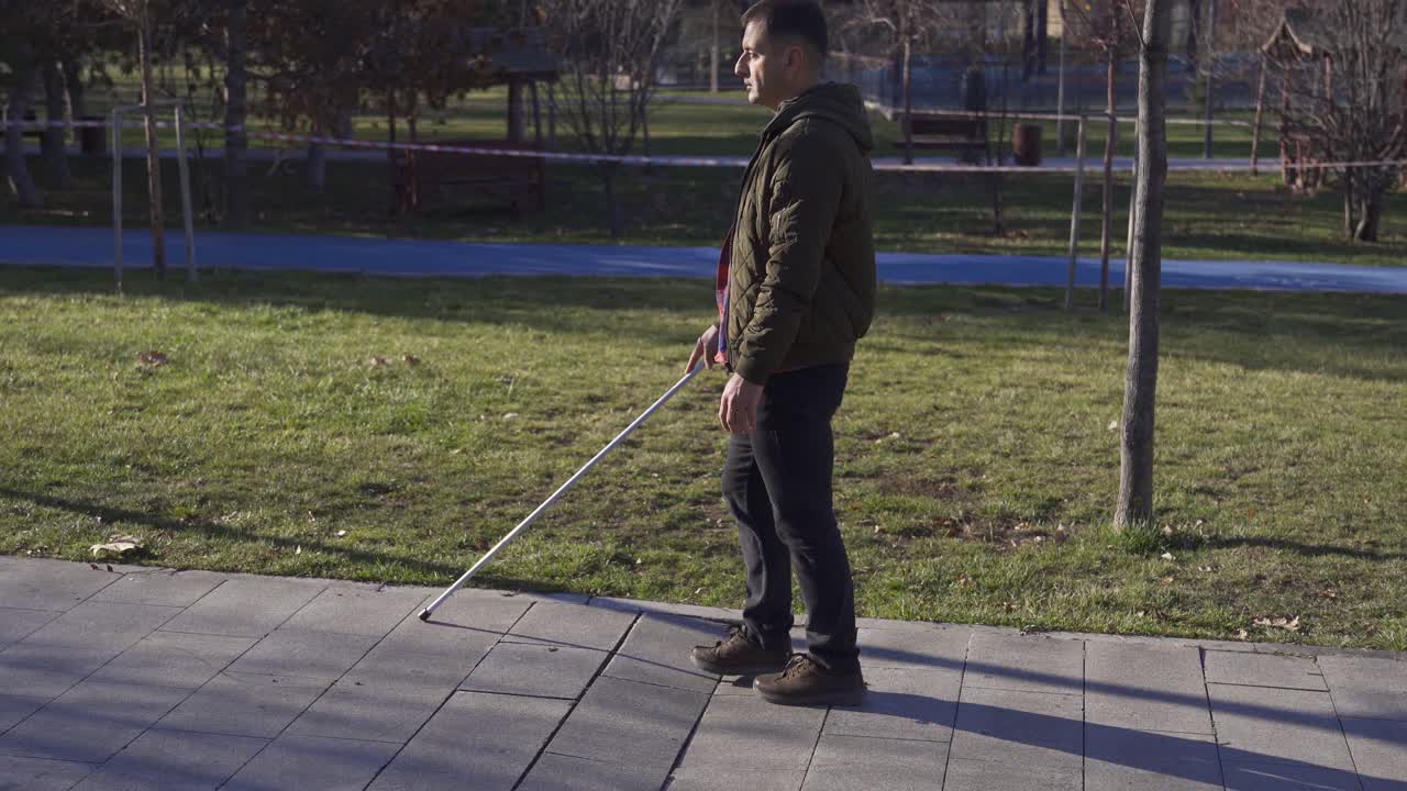 A blind man in a coat walking in the park in autumn.