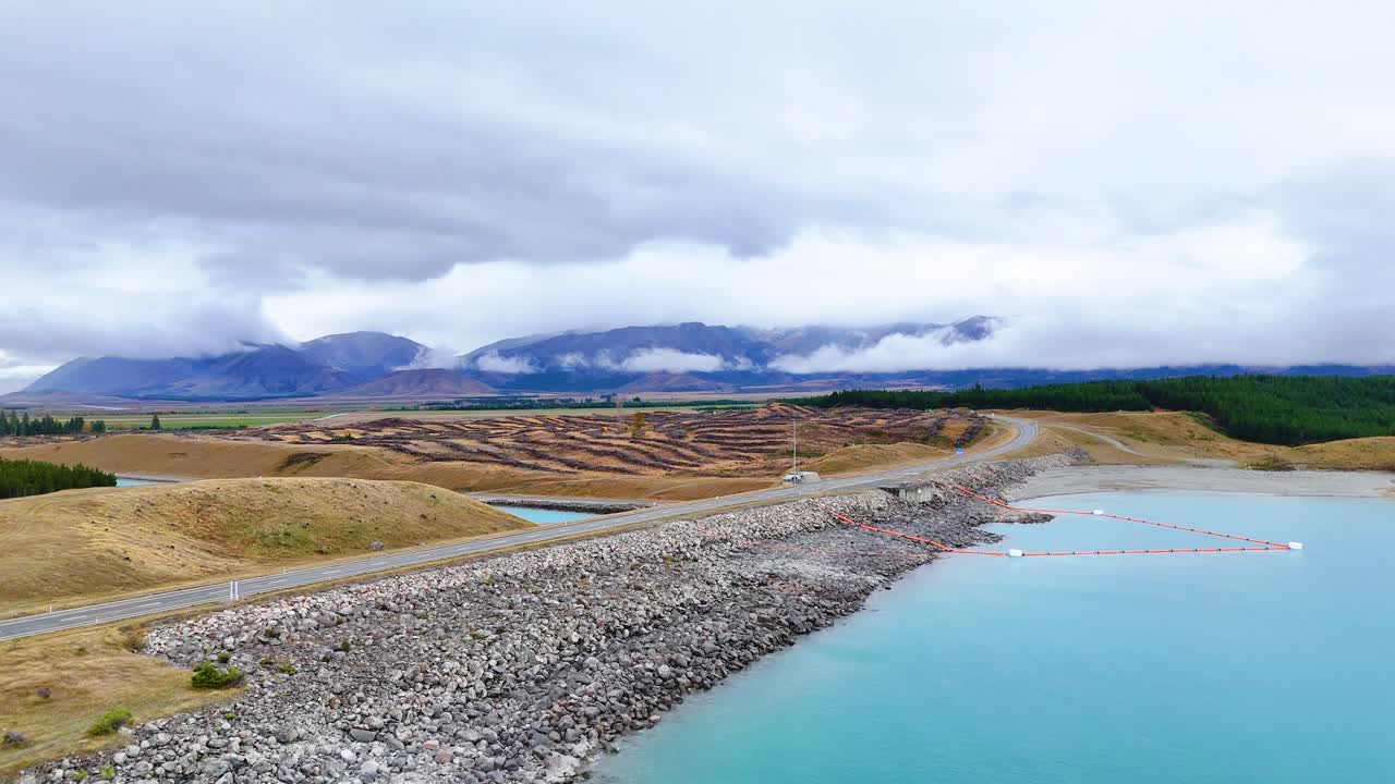 Aerial footage captures Lake Pukaki's turquoise waters and surrounding terrain under overcast skies, highlighting natural beauty and tranquility