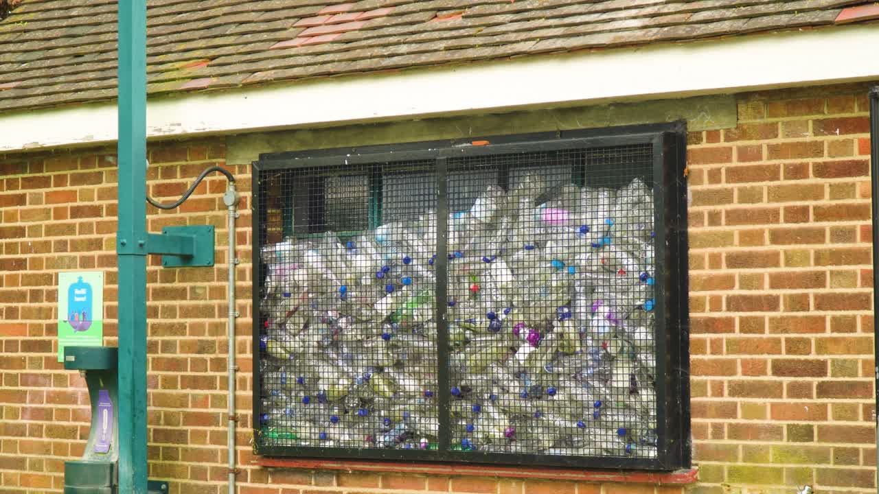 투명한 창문이 있는 건물 앞에 있는 물 충전 스테이션은 환경과 재활용의 필요성에 대해 관심을 갖지 않을 때  ⁇ 비되는 많은 플라스틱 병을 보여줍니다.