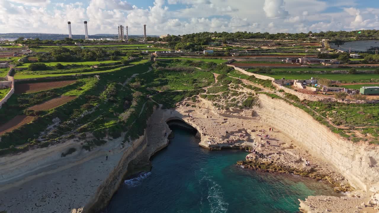 Vista aerea di St Peter's Pool a Malta, una baia rocciosa a forma di ferro di cavallo con acque mediterranee turchesi, scogliere calcaree e la campagna circostante, un famoso punto di riferimento costiero vicino a Marsaxlokk