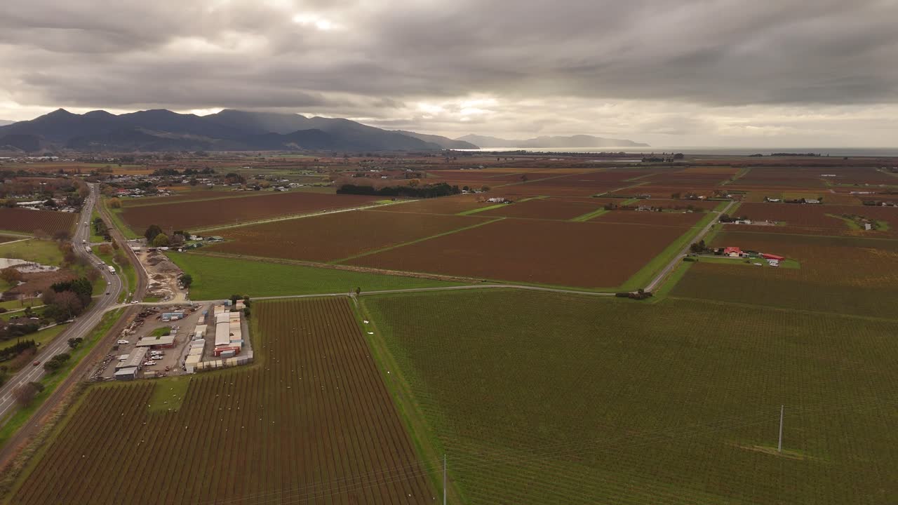Traffic on intersection road betwe. Farm fields of Blenheim, New Zealand. Dark clouds at sky in summer. Rural area countryside with mountains in distance. Aerial wide shot