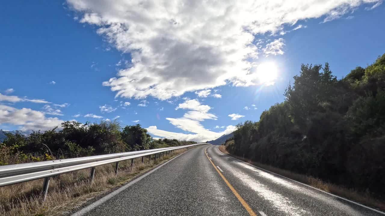 Car travels sunlit rural highway, lush greenery, dynamic clouds, wide angle, smooth forward motion