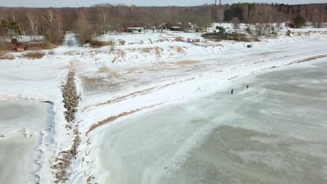 drone view of snow covered beach, closing in on people walking on shore