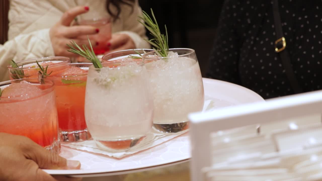 Woman taking gin and tonic drink from tray carried by waiter at party