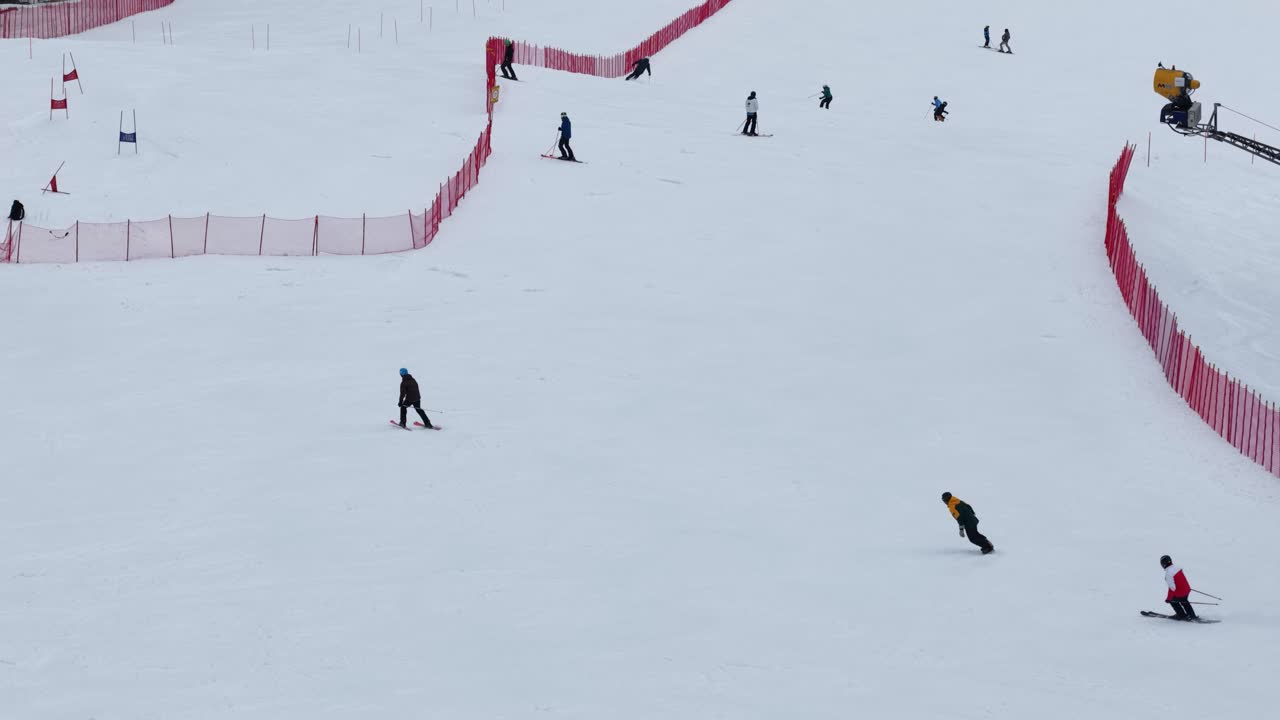 Aerial drone footage of skiers and snowboarders descending a snowy ski slope in Folgaria, Trentino, Italy, captured with a telephoto lens to highlight speed and dynamic action