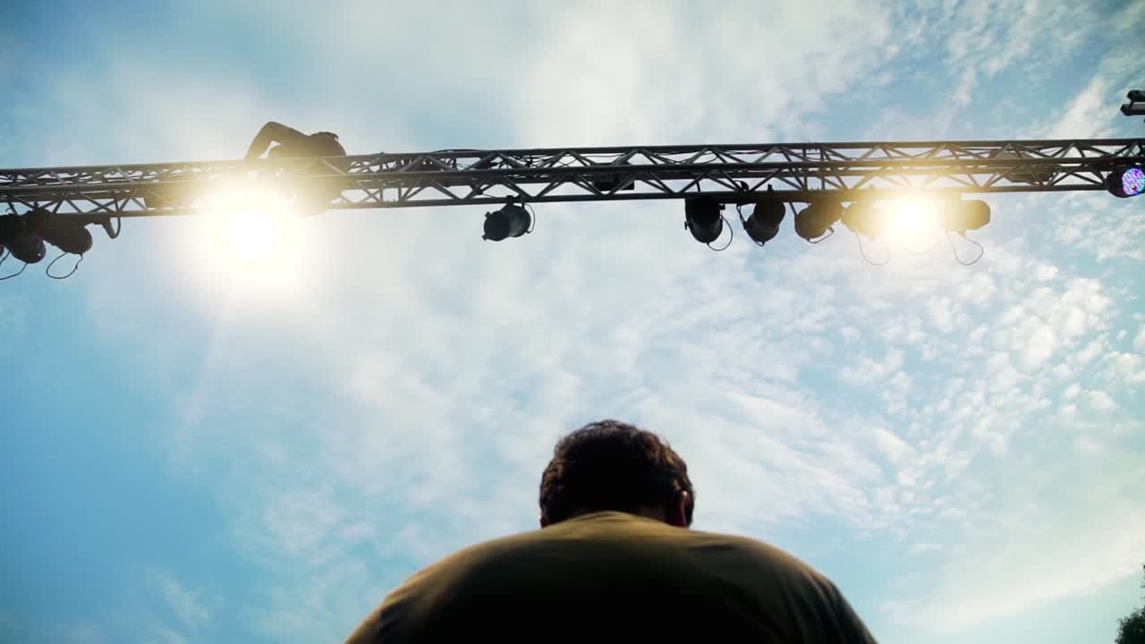 day shot of the back of a man sitting, standing under hanging concert lights