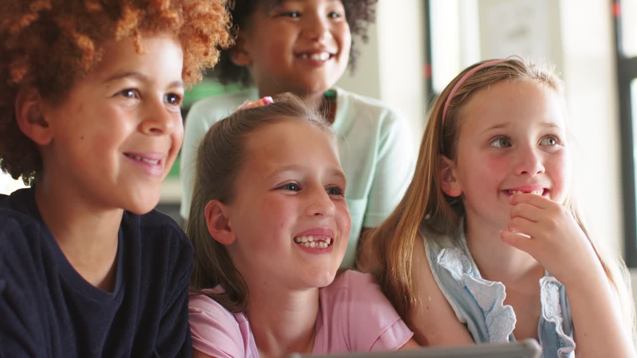 Eine vielfältige Gruppe von Kindern, die sich einem Tablet zuwendet, um einen lustigen Clip in der Schule anzusehen, zuschaut und lacht