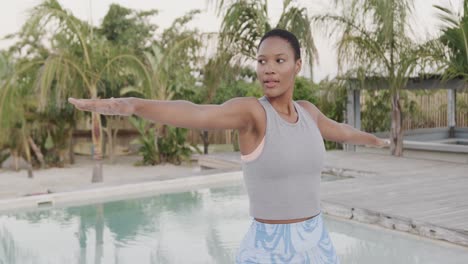 happy biracial woman practicing yoga, standing with arms outstretched on beach, slow motion