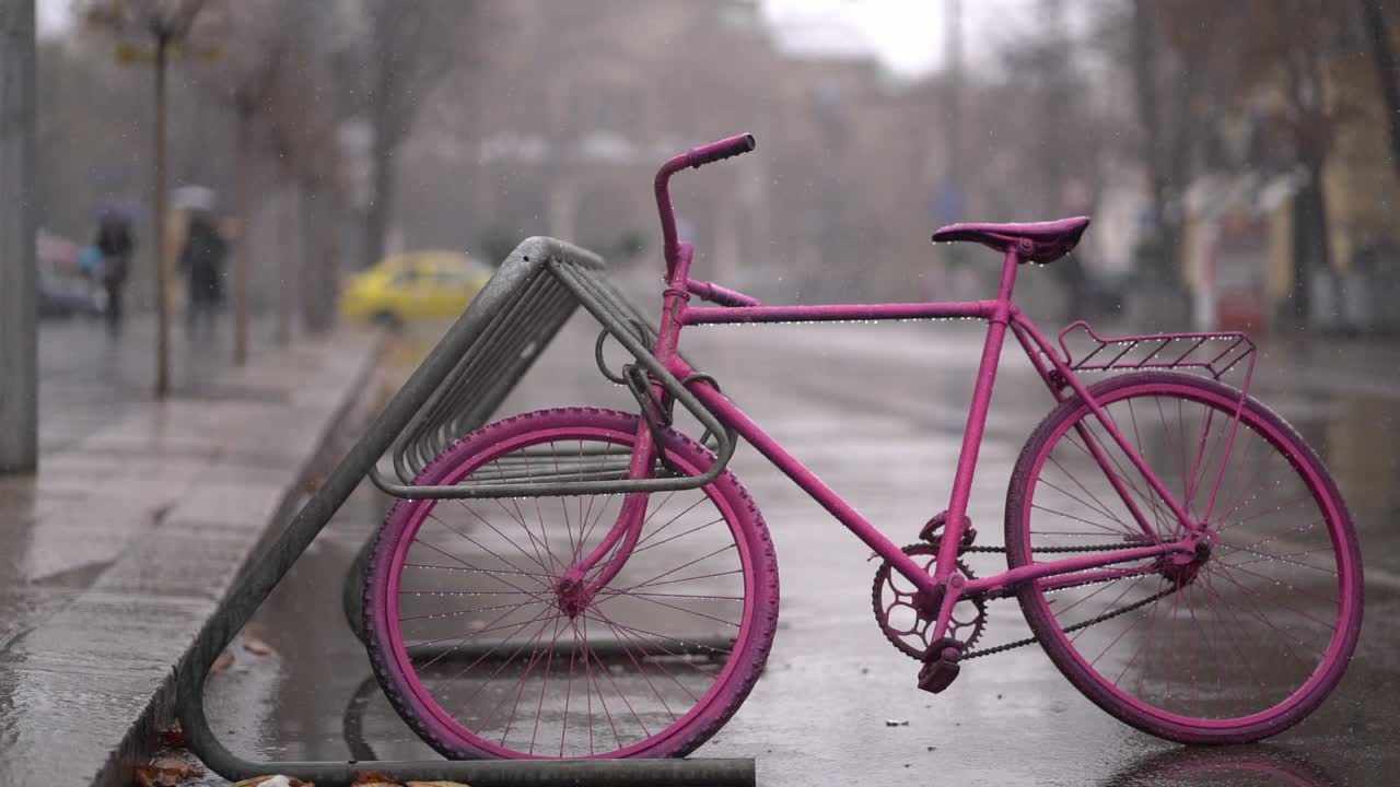 Pink singlespeed bicycle locked up against bike rack on wet cold day in Bulgaria