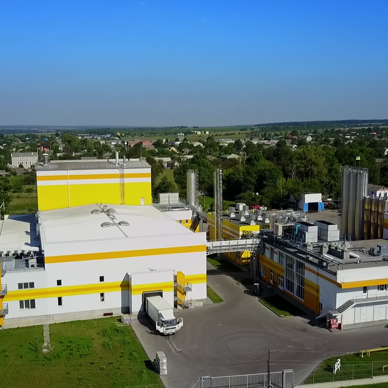 A truck moving out from the factory premises. Private houses and lots of greenery surrounding the industrial plant. Top view