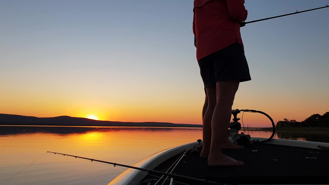 pesca de lubina en un hermoso lago tranquilo con la puesta de sol a lo lejos