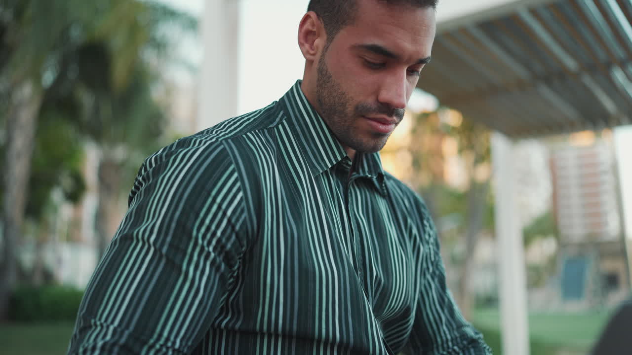 giovane uomo che usa il portatile seduto in panchina all'aperto.