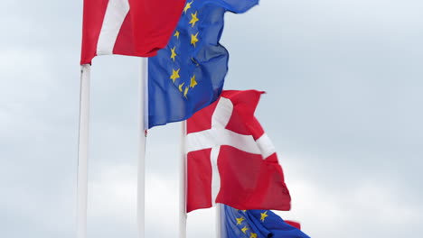 close up gimbal shot of danish and european union flags against cloudy sky