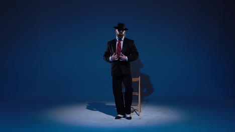 man in suit and hat posing under spotlight on blue background