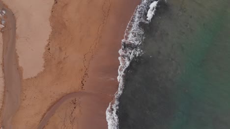 Flying-above-turquoise-ocean-waves-washing-the-empty-sandy-beach