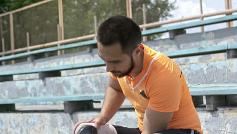 Amputee-Athlete-Sitting-On-Stadium-Bleachers-And-Putting-On-Running-Blade-Before-Training