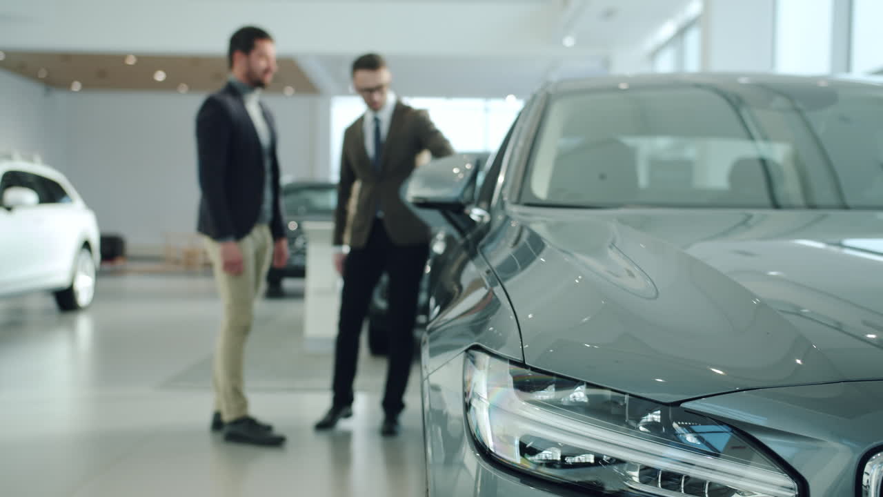 Car Salesman Showing a Grey Sedan to a Customer in a Showroom