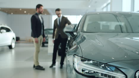 car salesman showing a grey sedan to a customer in a showroom