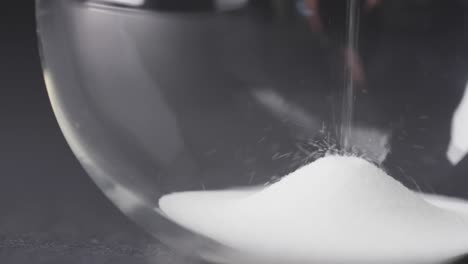 Video-of-close-up-of-hourglass-with-sand-pouring,-copy-space-on-black-background