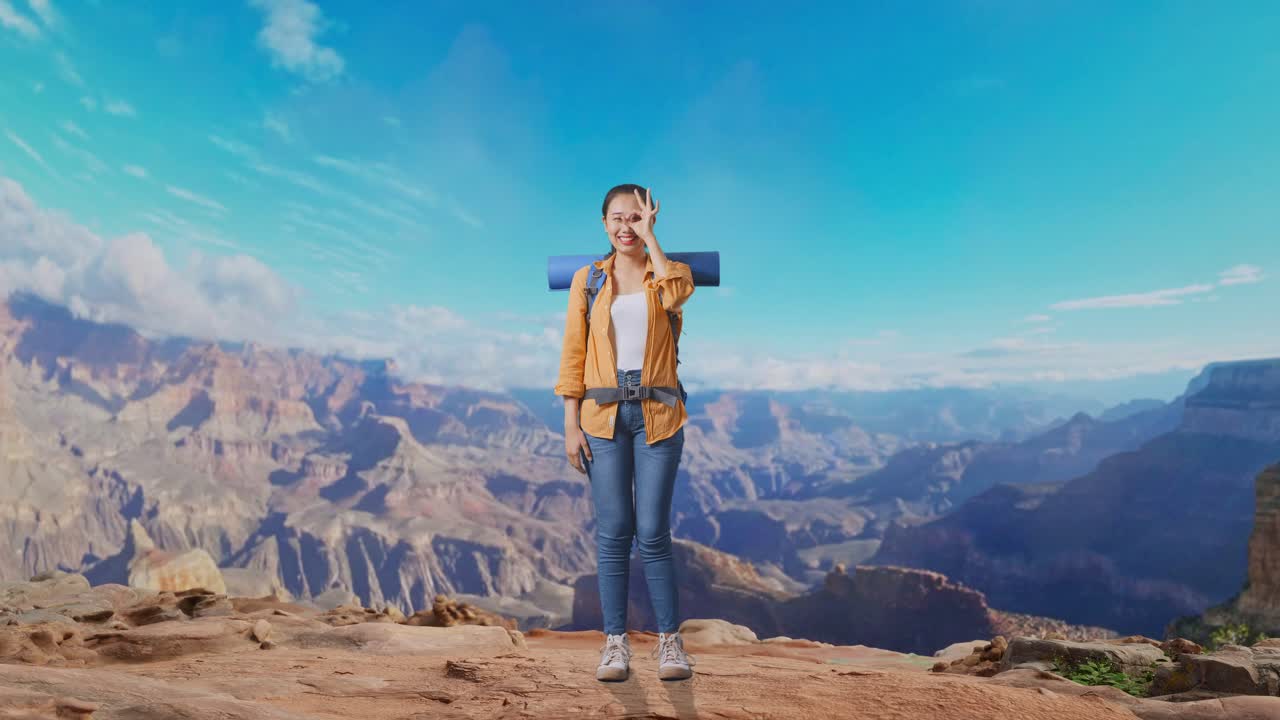 Full Body Of Asian Female Hiker With Mountaineering Backpack Smiling And Showing Ok Sign With Fingers Over Eyes While Traveling At The Top Of Mountain