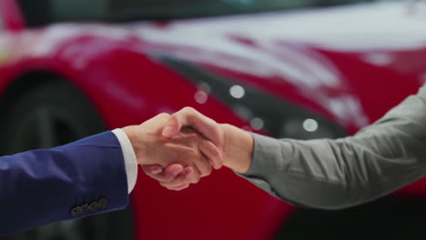 una pareja feliz con un atractivo concesionario de automóviles en un traje presentando un nuevo modelo de coche a su cliente, estrechar la mano con el vendedor y tomar la llave del coche nuevo