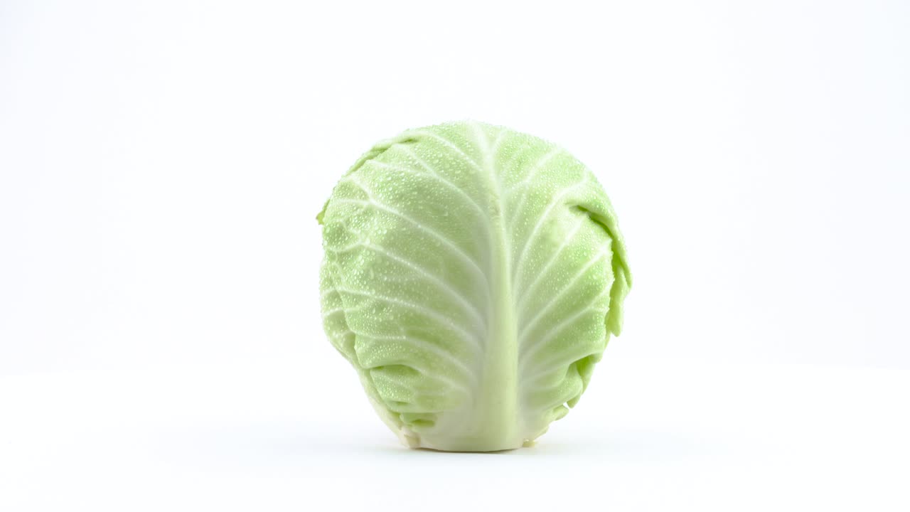 una mini repollo blanco entero con gotas de agua está girando en la mesa giratoria aislada en el fondo blanco. primer plano. macro.