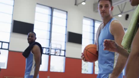 happy diverse male basketball team bouncing balls and talking on indoor court, slow motion