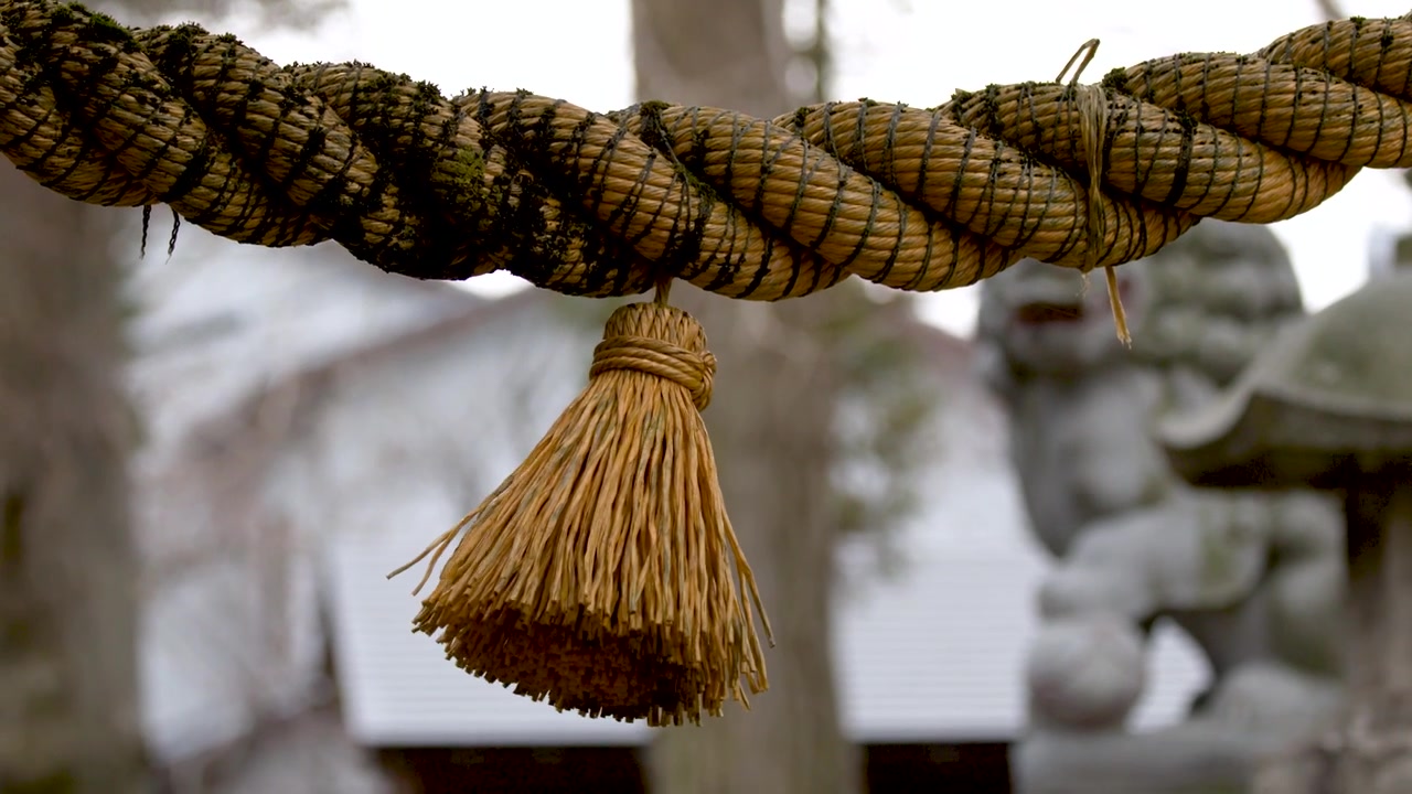 Eine Nahaufnahme mit Kameraneigung enthüllt ein heiliges Shinto-Shimenawa-Seil und eine Quaste an einem Schrein