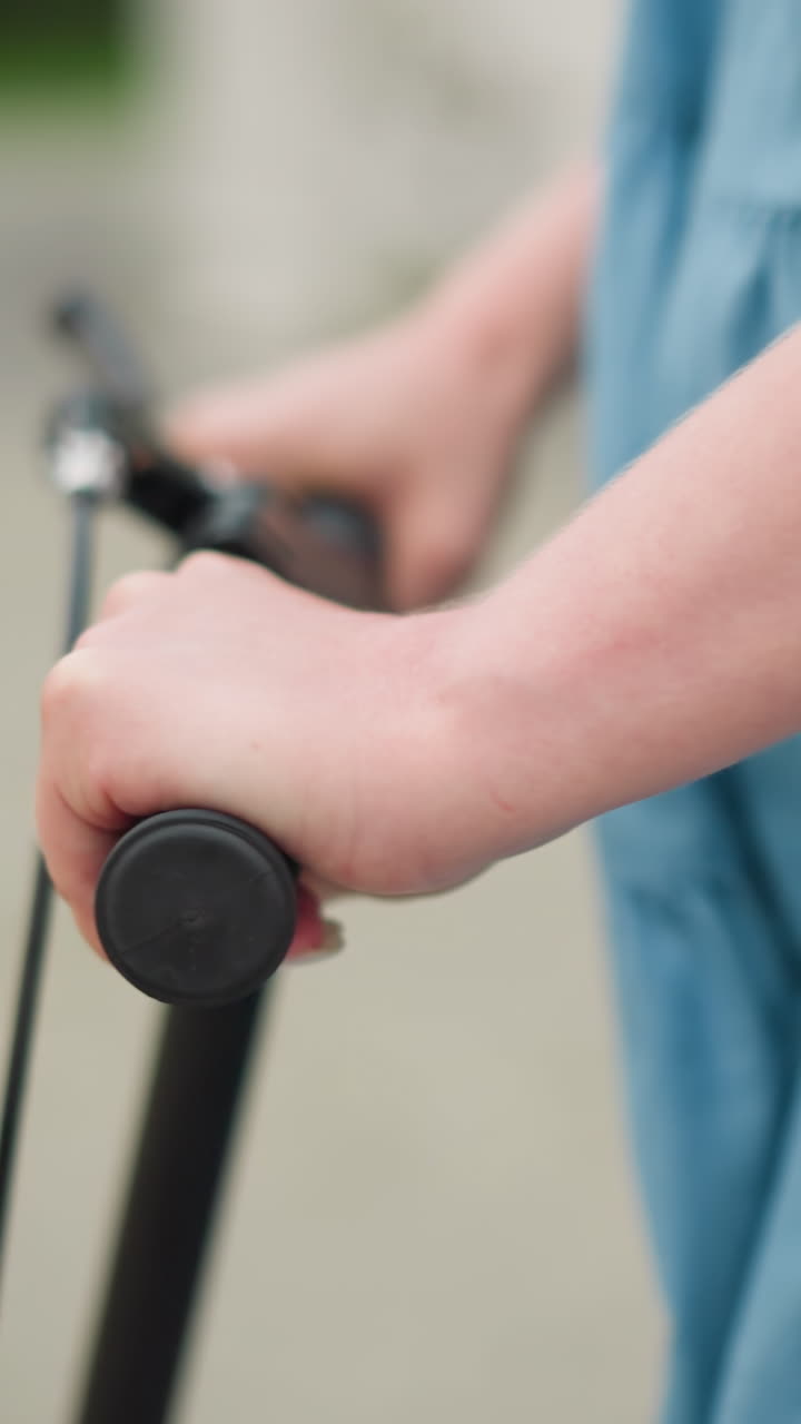 un primer plano de las manos de una mujer agarrando firmemente y dirigiendo un scooter mientras se impulsa hacia adelante, en el fondo borroso, se puede ver a una persona montando una bicicleta