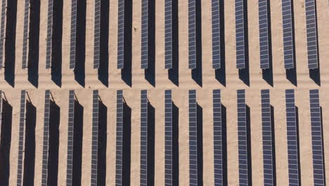 rows of solar panels at a solar farm in a desert during daytime, aerial top down