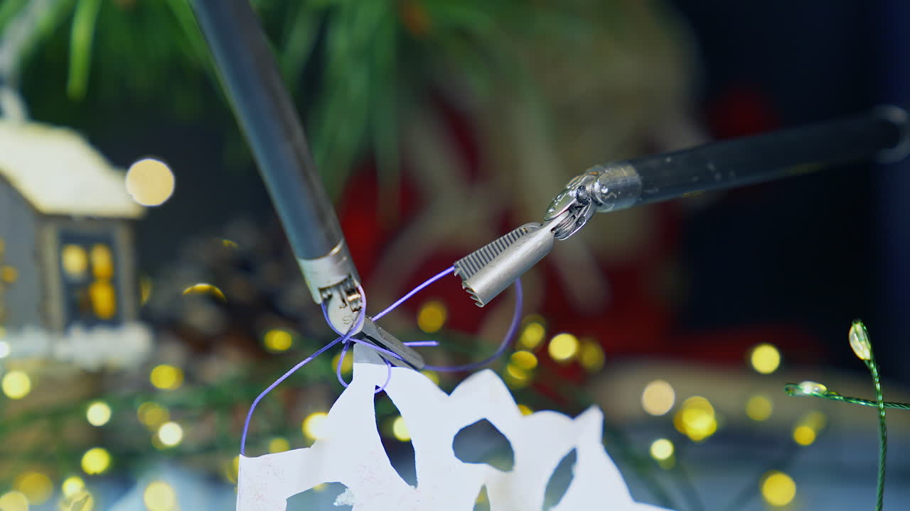 Tiny claws of the robotic arms tying the thread to the paper snowflake. Precise movements of the equipment. Christmas decorations at the backdrop.