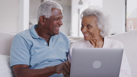 senior couple sitting on sofa at home using laptop together