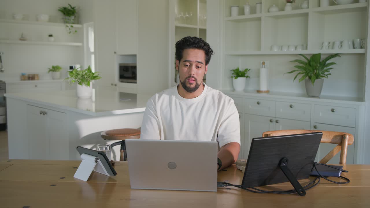 Homem começando a trabalhar remotamente no laptop, digitando e olhando para o monitor externo, depois se alongando
