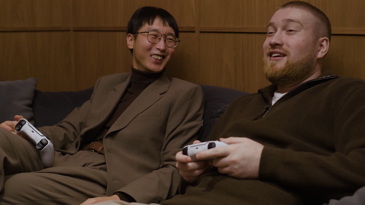 두 남자가 소파에서 비디오 게임을 하고 있다.