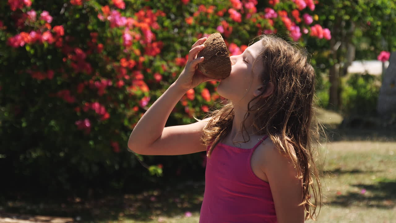 신선하고 갈라진 껍질에서 코코넛 물이나 우유를 마시는 귀엽고 초반 소녀