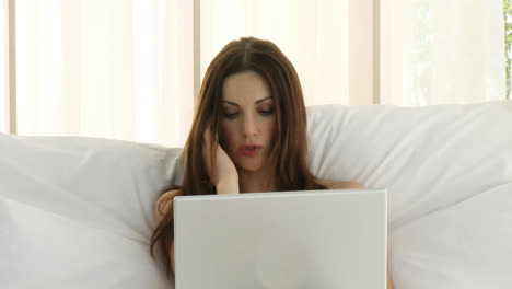 close up of a woman using a laptop and talking on phone in bed