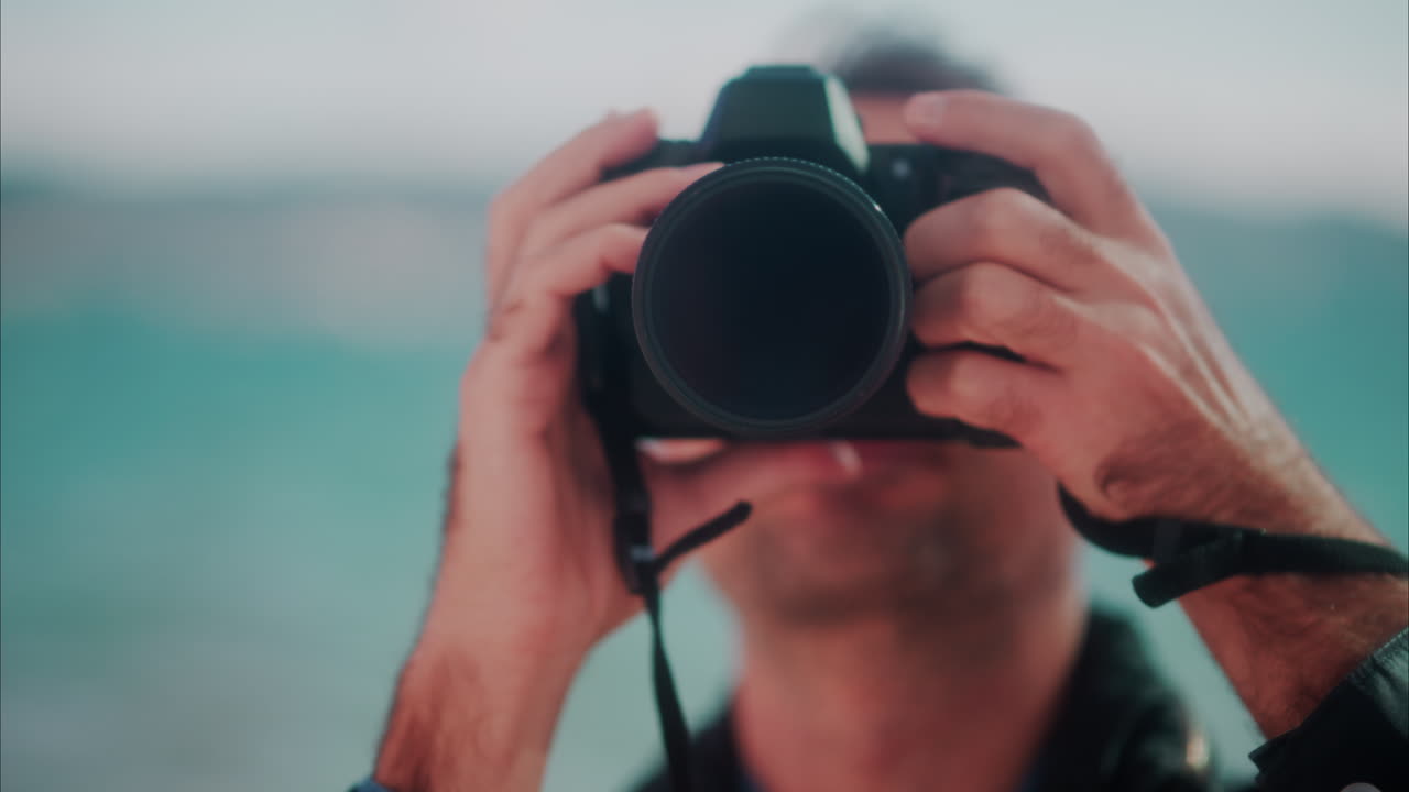 Close up of a man taking pictures with a blurry view of the sea on the background