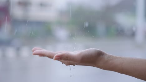 rain drops to female light skin hand, rainy day with car driving pass on the background, under heavy rain close up, catches rains on palm, rainy season in slow motion, standing on the street side