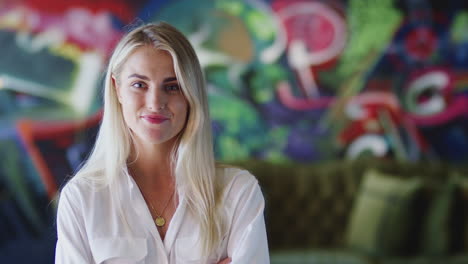 Young-white-female-creative-smiling-to-camera-in-front-of-mural-in-casual-office,-head-and-shoulders