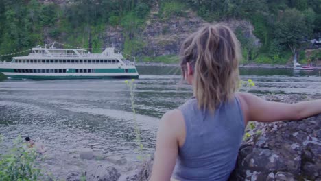 cute hipster girl watching a cruise ship go by from the edge of the water