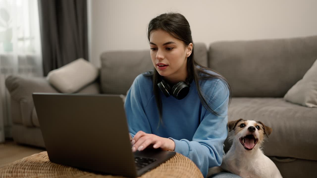 mujer joven con auriculares sentada en el suelo con su perro trabajando en una computadora portátil