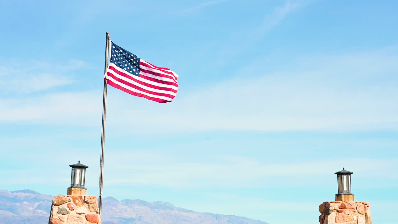 Bandiera americana sventolata dal vento con due pali ai lati e sfondo di cielo blu